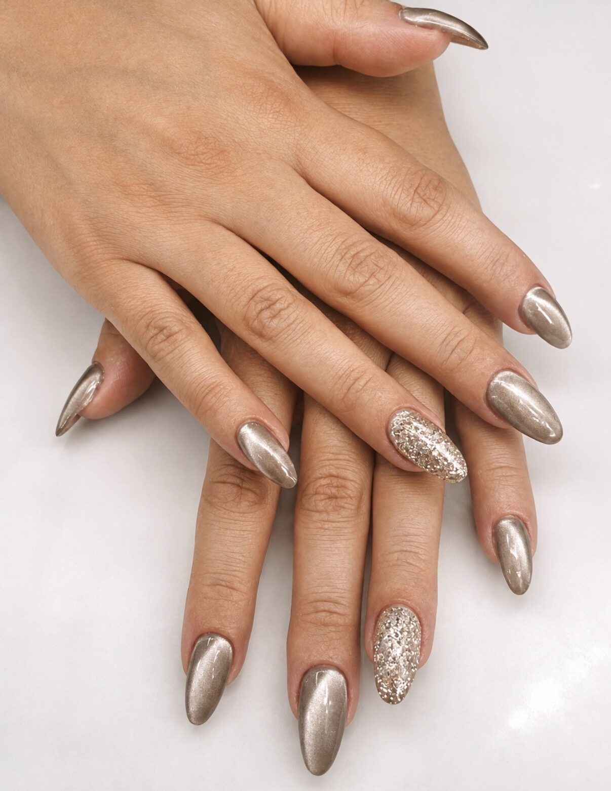 Uñas almendradas largas en chrome champán dorado, dos uñas con purpurina a juego.