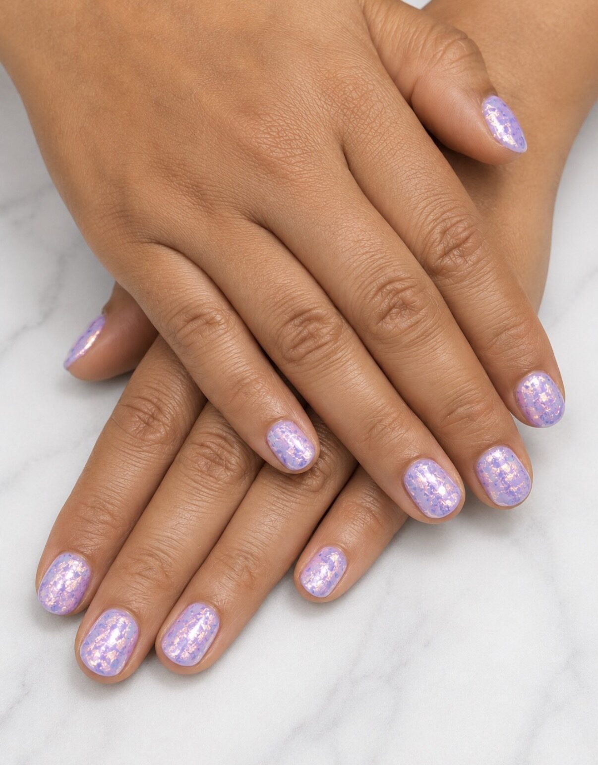 Uñas cortas cubiertas por un velo irisado lila con purpurina fina.