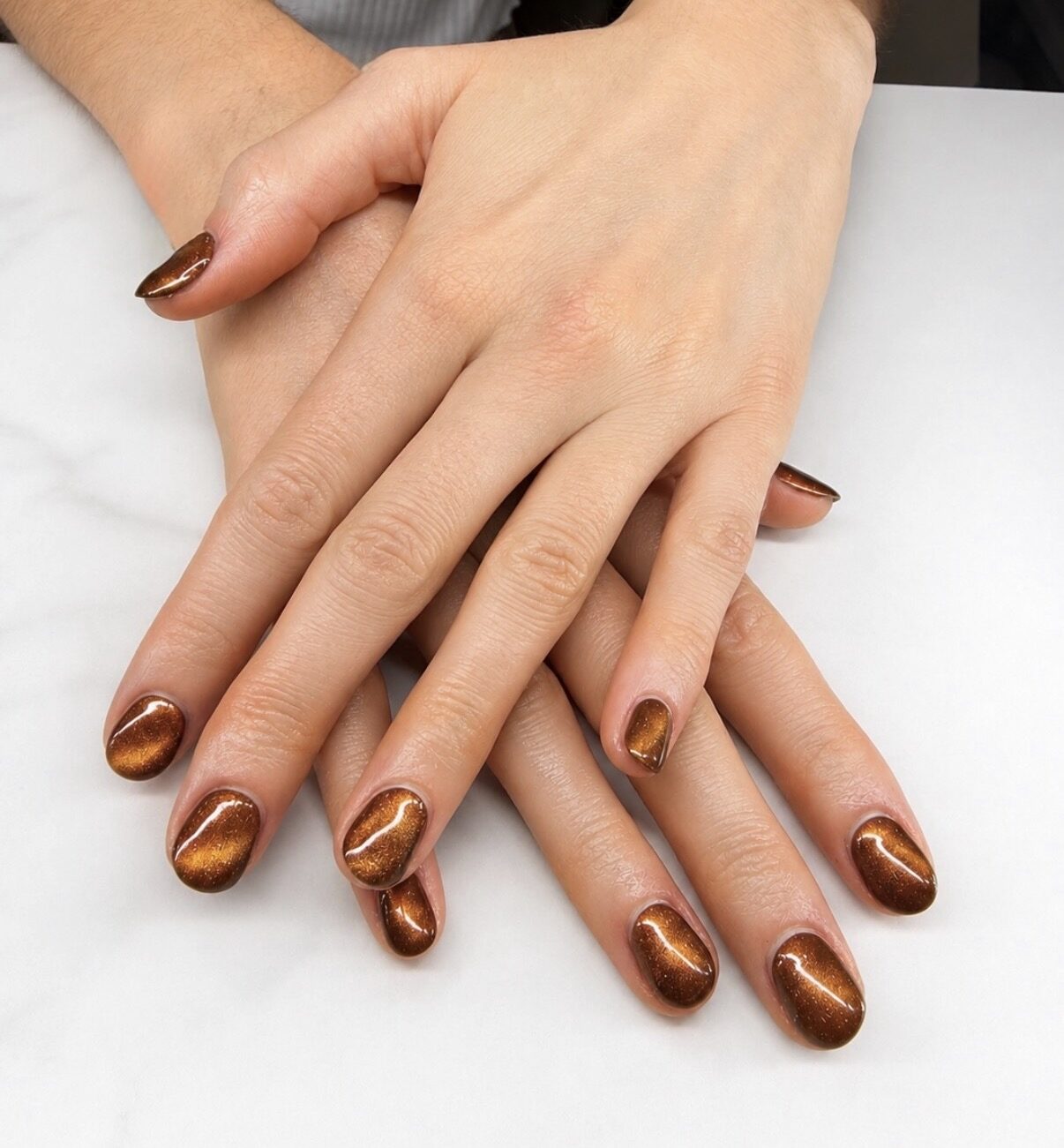 Uñas cortas en cat eye cobrizo, reflejo que se mueve con la luz.