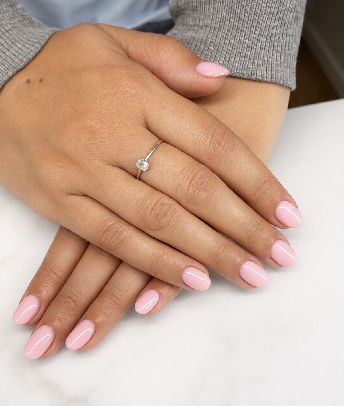 Uñas almendradas rosa pálido lechoso, acabado brillante, sobre mármol blanco.