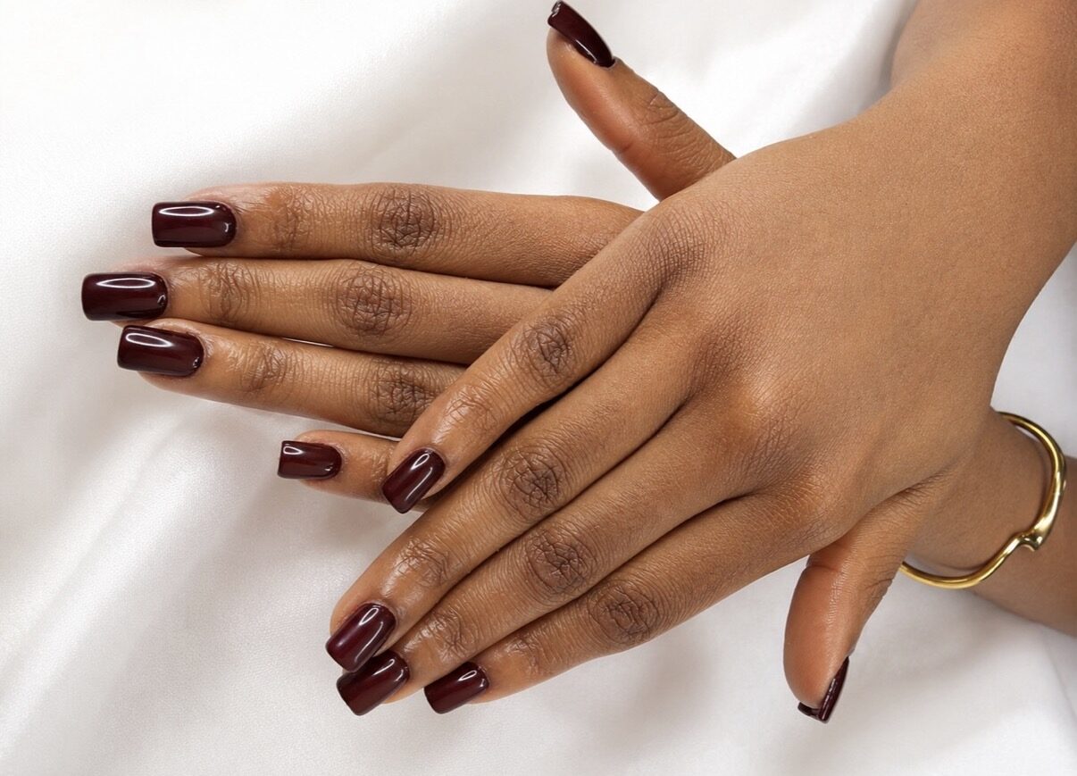 Uñas largas cuadradas burdeos chocolate, sobre tela blanca.